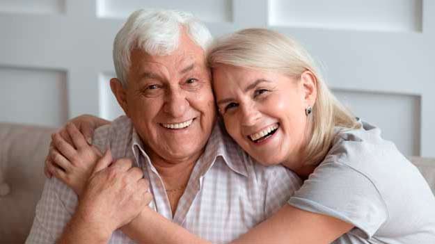An elderly couple with bright smiles, showcasing their happiness with dentures in Guildford
